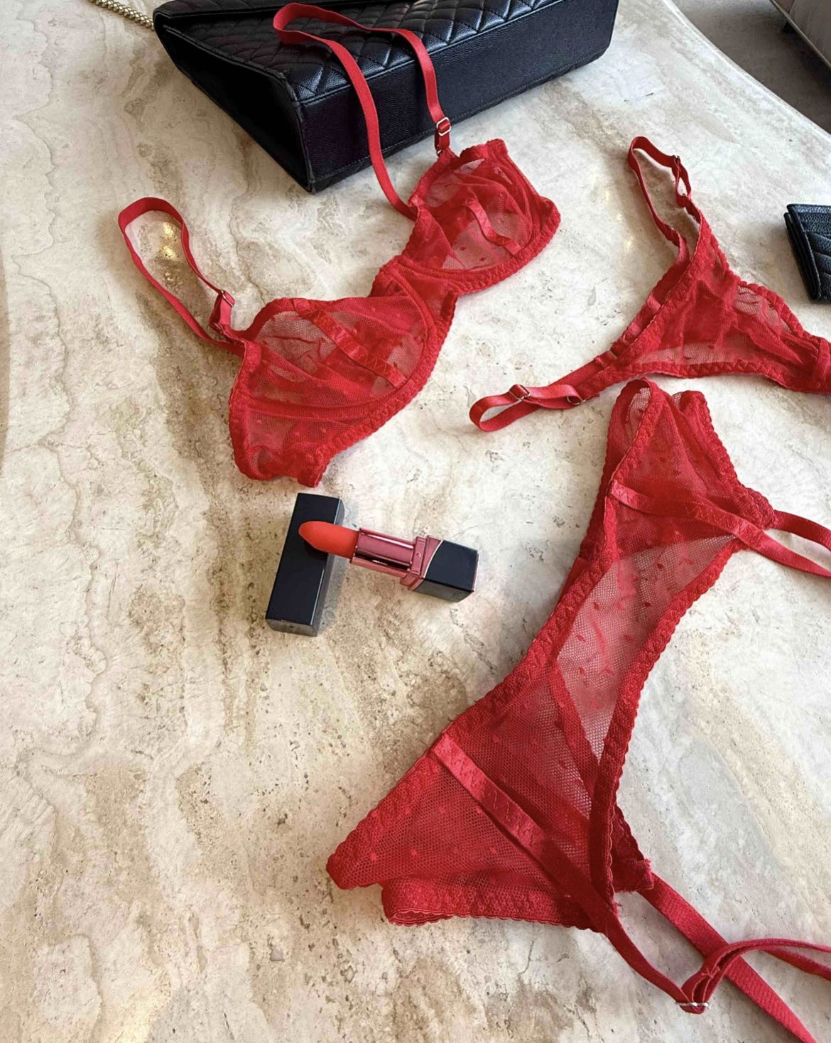 Red sheer mesh lingerie set with bra and thong styled on marble surface with black quilted bag and red lipstick, curated Valentine look by SELF Seductions.
