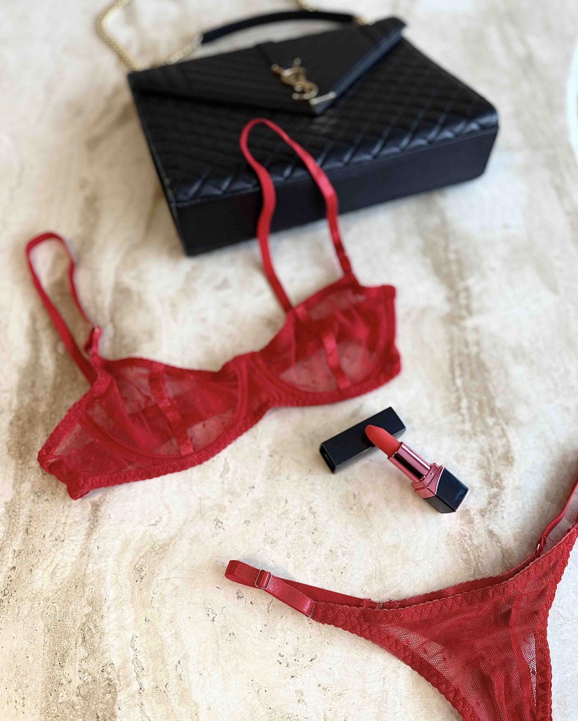 Red sheer mesh lingerie set with bra and thong styled on marble surface with black quilted bag and red lipstick, curated Valentine look by SELF Seductions.