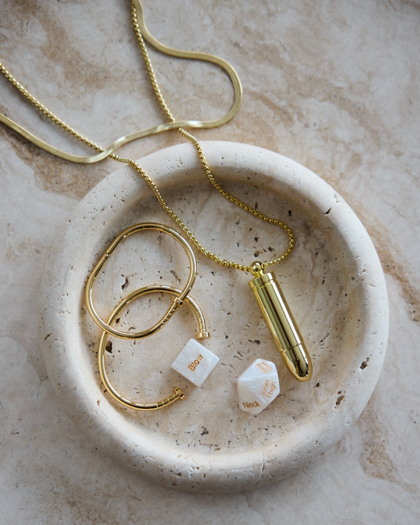 Gold undercover necklace styled with sensual dice in marble dish – refined and intimate aesthetic