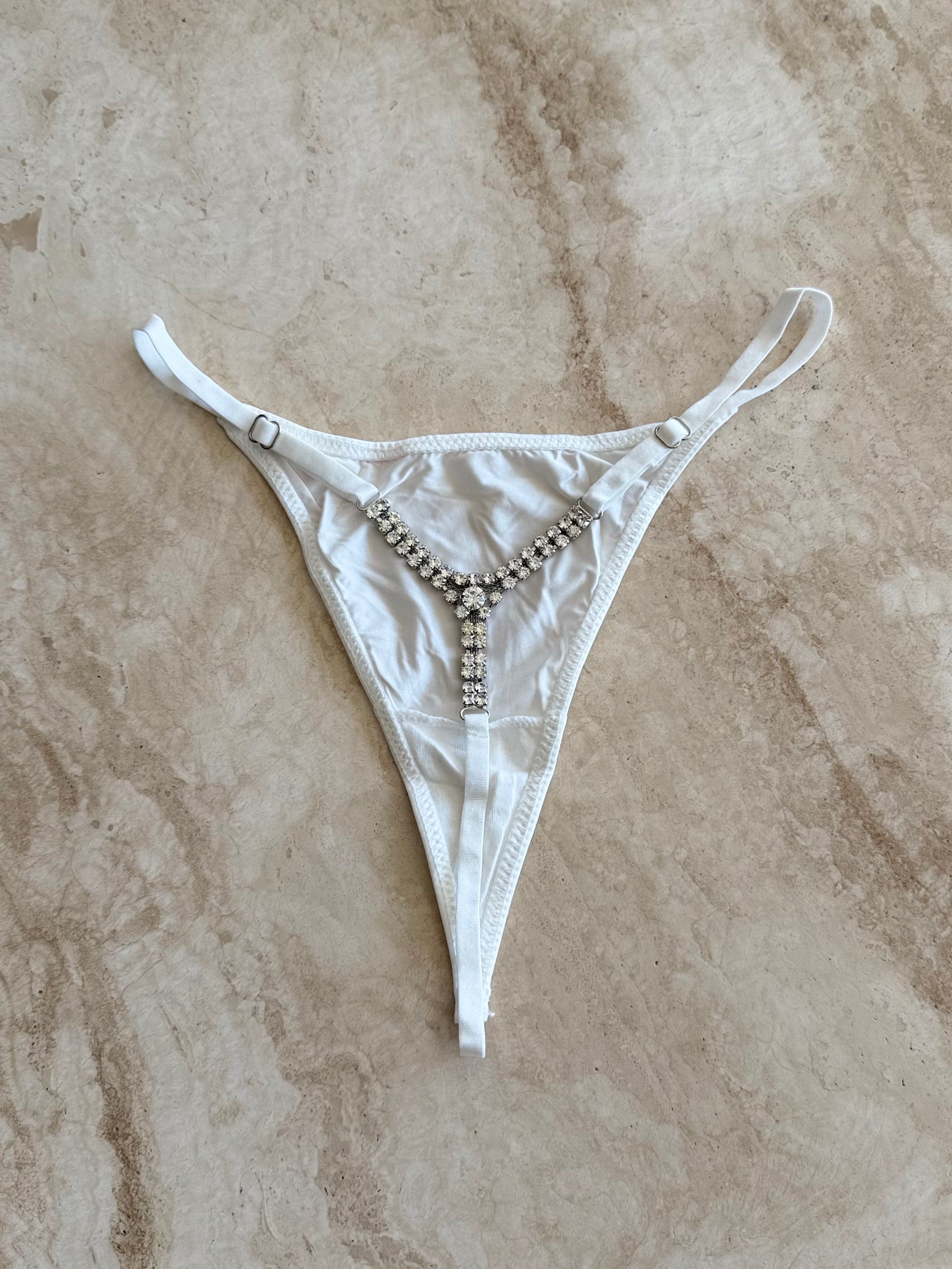 White crystal-embellished thong displayed on soft beige marble – elegant lingerie by SELF Seductions