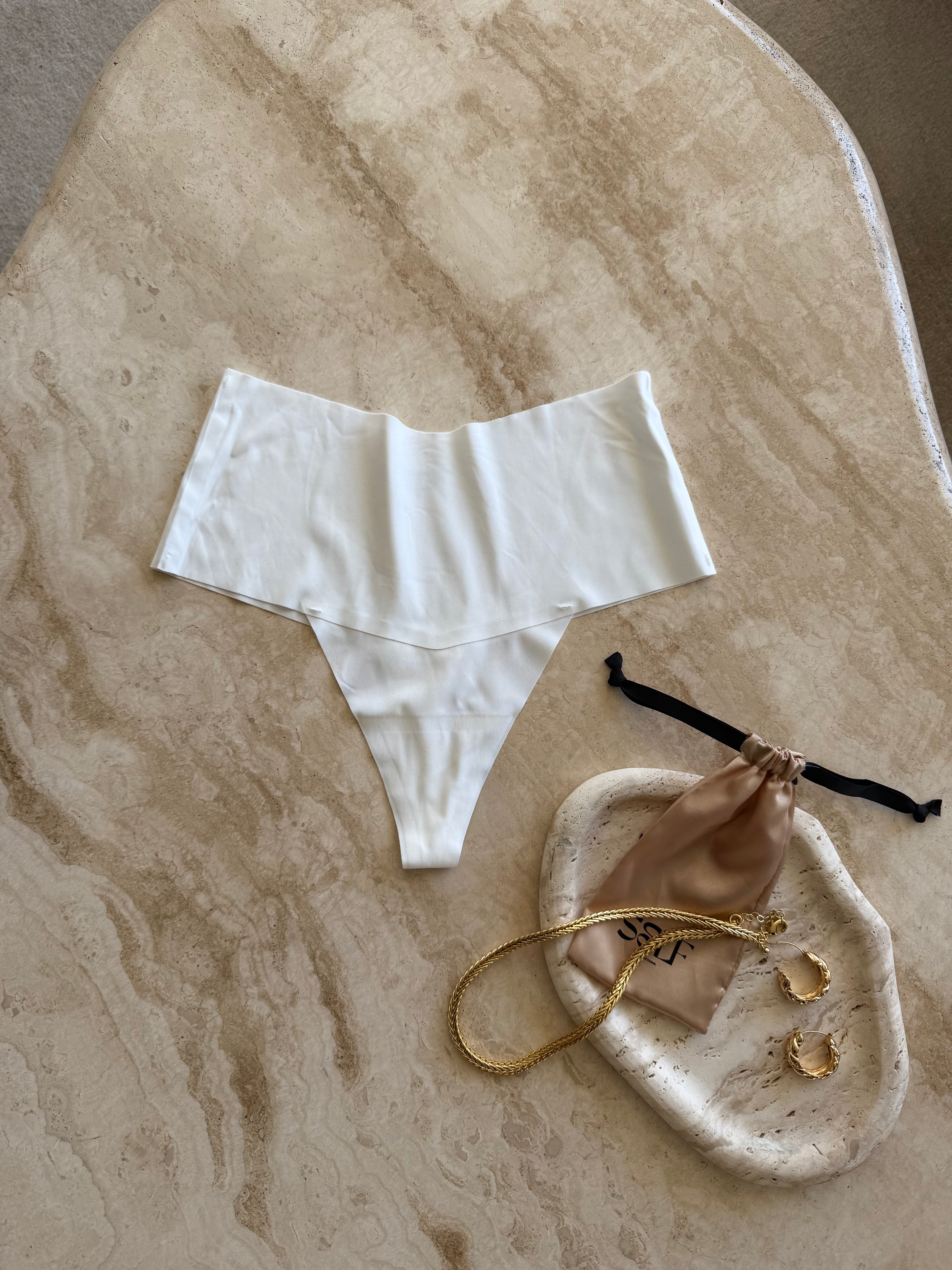 The Kourtney Seamless Sports High Waist Thong in white styled with delicate jewelry on soft marble surface – elegant and refined flatlay by SELF Seductions