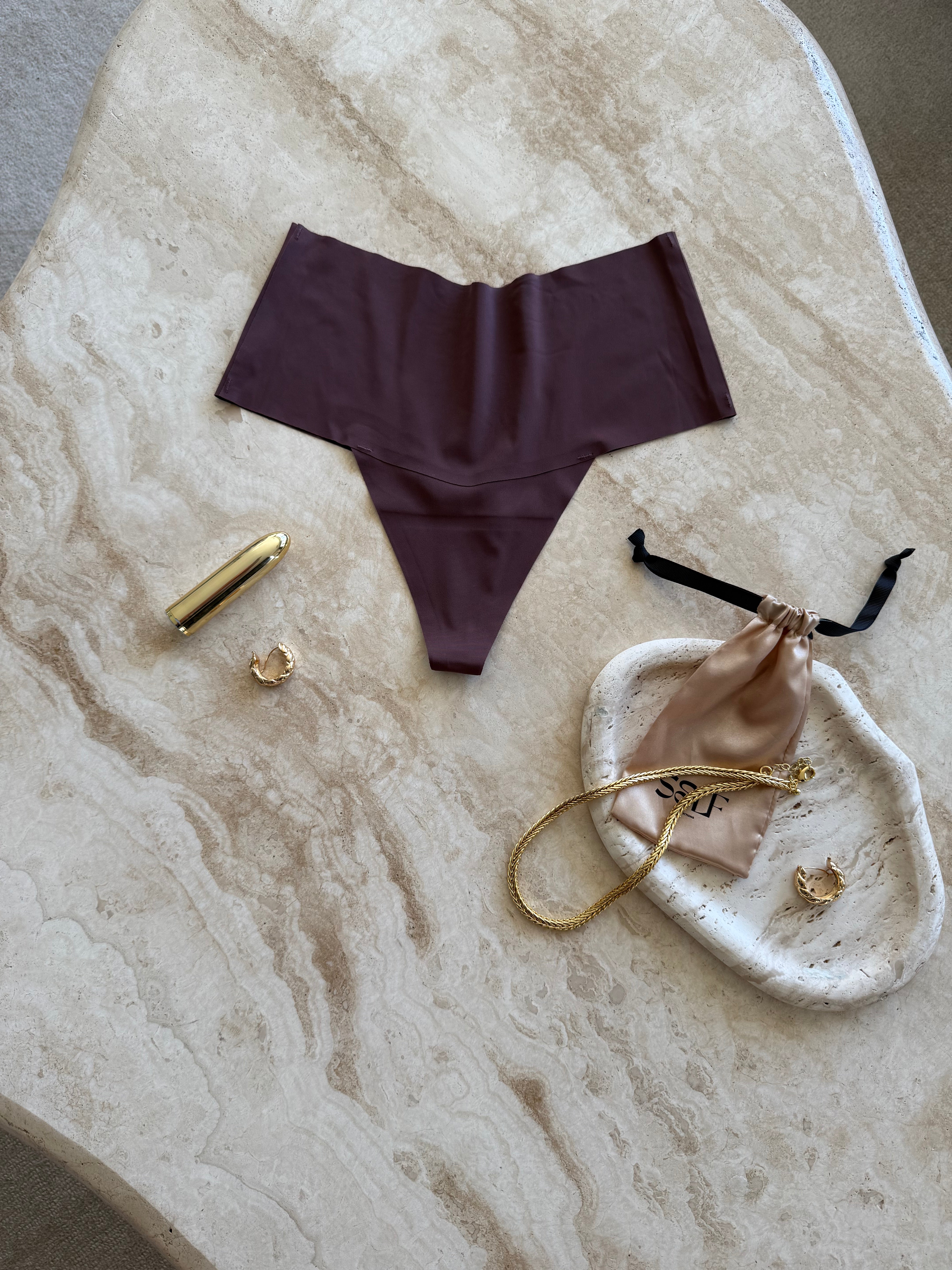 The Kourtney Seamless Sports High Waist Thong in chocolate brown styled with gold jewelry on marble surface – minimalist still life by SELF Seductions