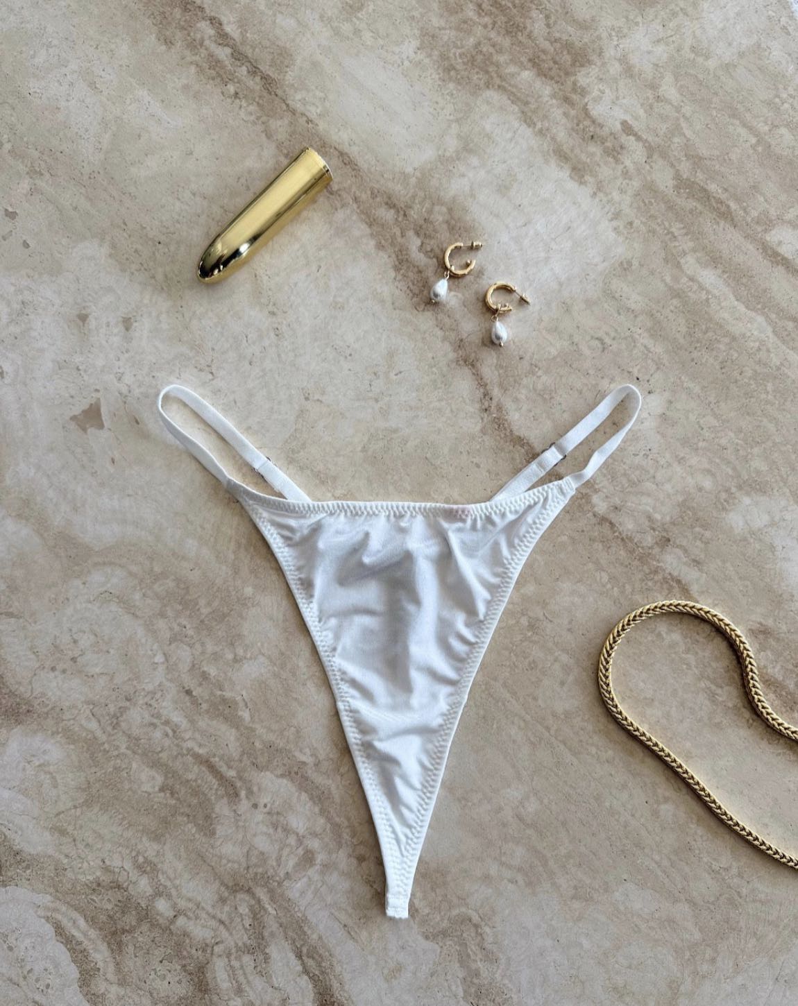 The Lilly Crystal V Thong in white styled with gold jewelry on marble surface – sensual flatlay by SELF Seductions
