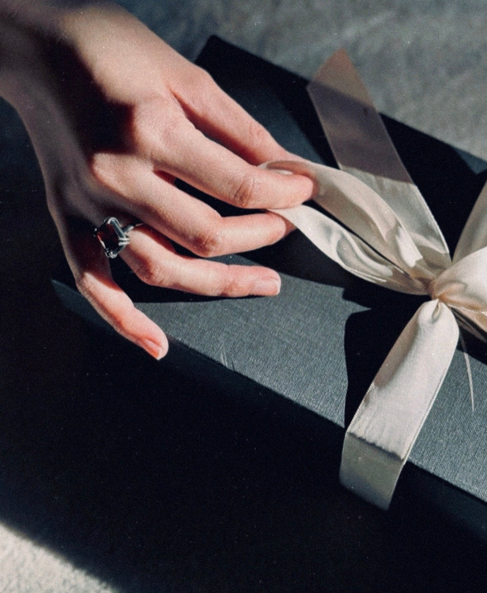 A hand gently touching a ribbon on a black gift box in soft light.