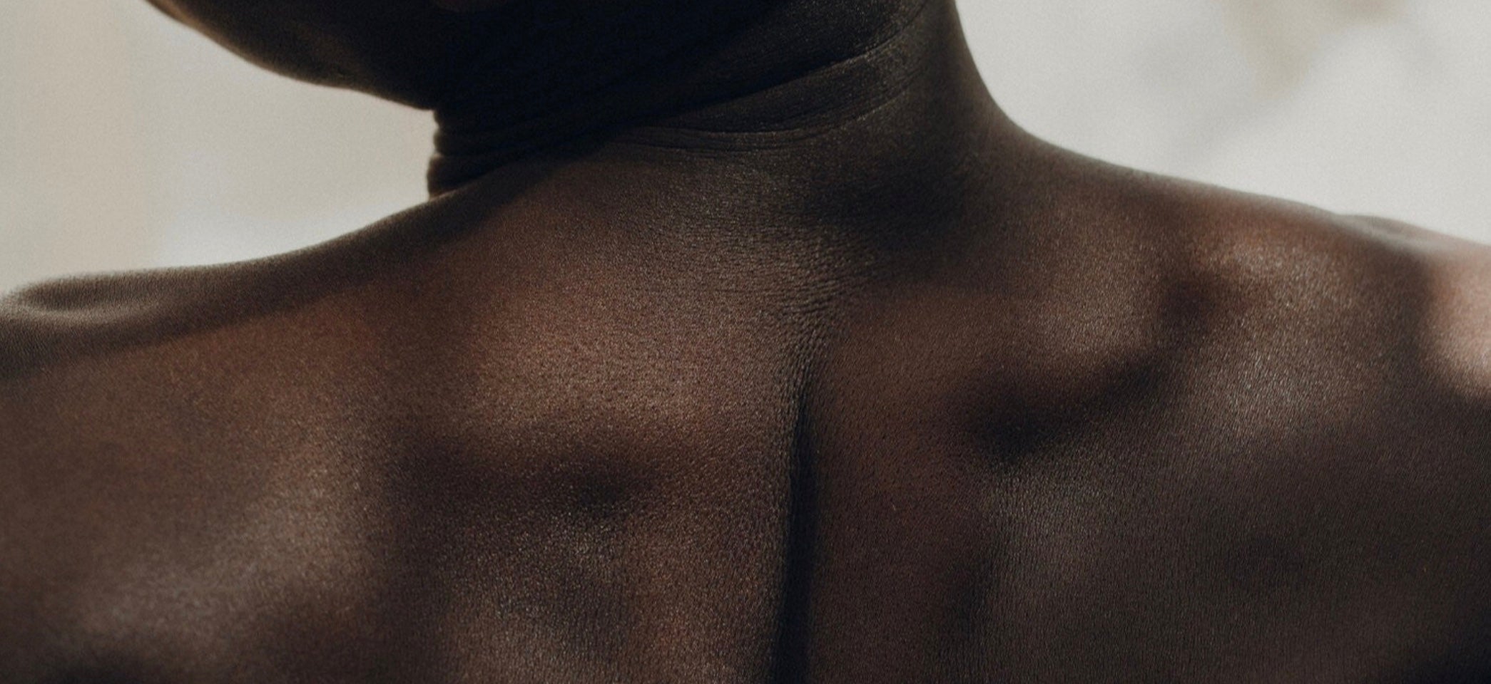 Close-up of a person's back and shoulders with soft light and smooth skin texture.