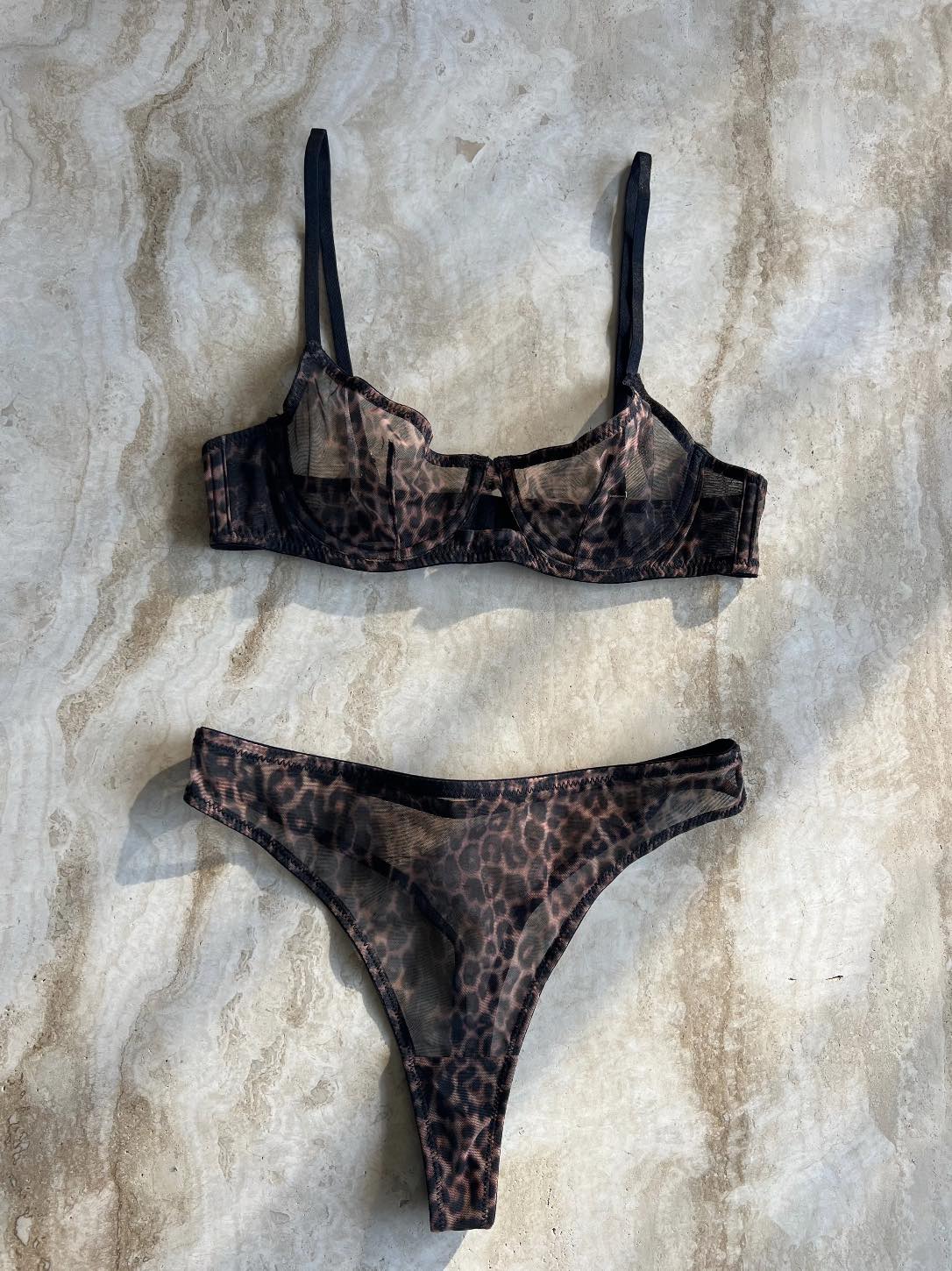 The Yves Leopard Mesh Set in sheer leopard print mesh, featuring a structured brassiere and matching thong on a textured stone surface.
