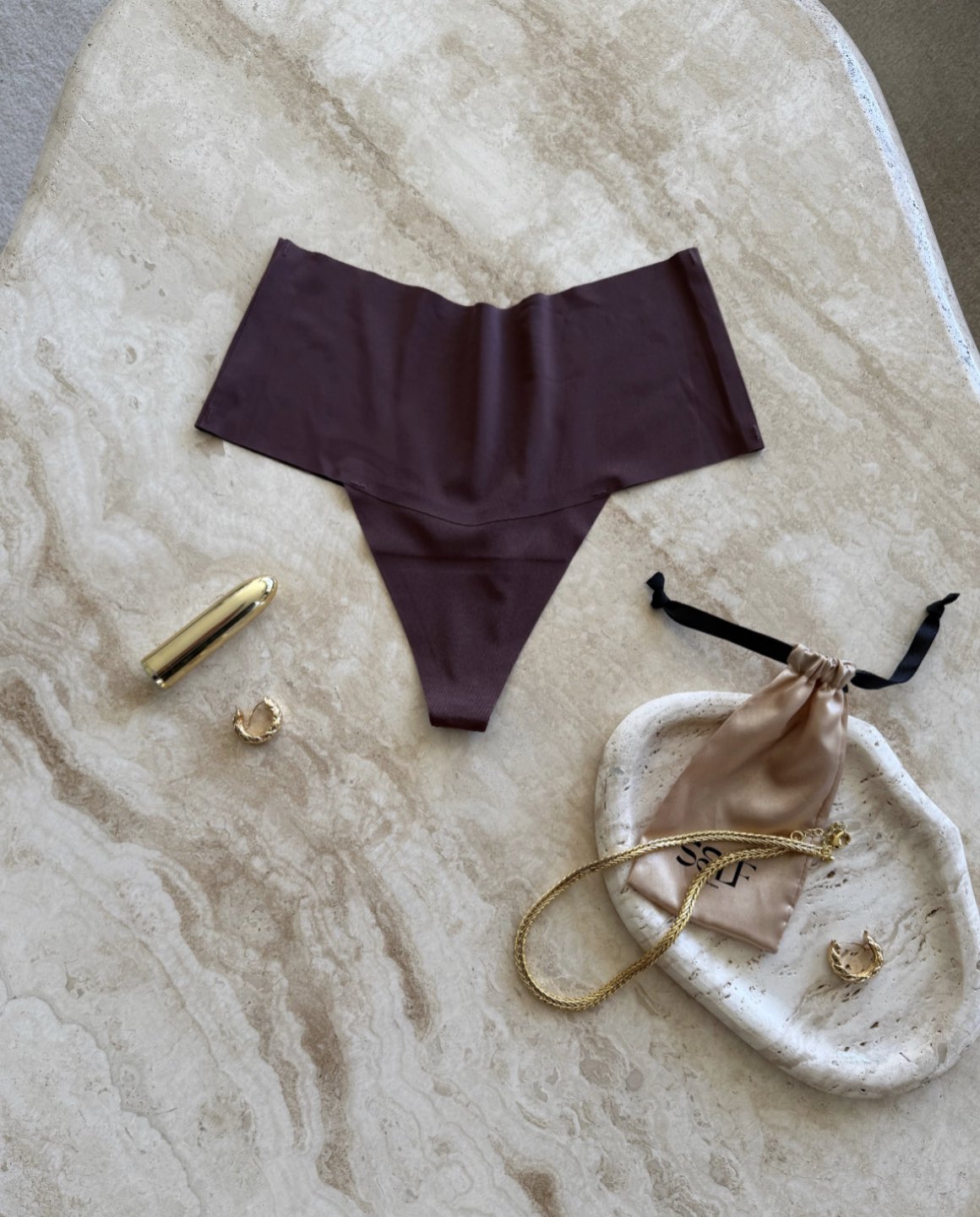 Detail view of The Kourtney Seamless Sports High Waist Thong in chocolate brown styled with gold jewelry on marble surface – minimalist still life by SELF Seductions
