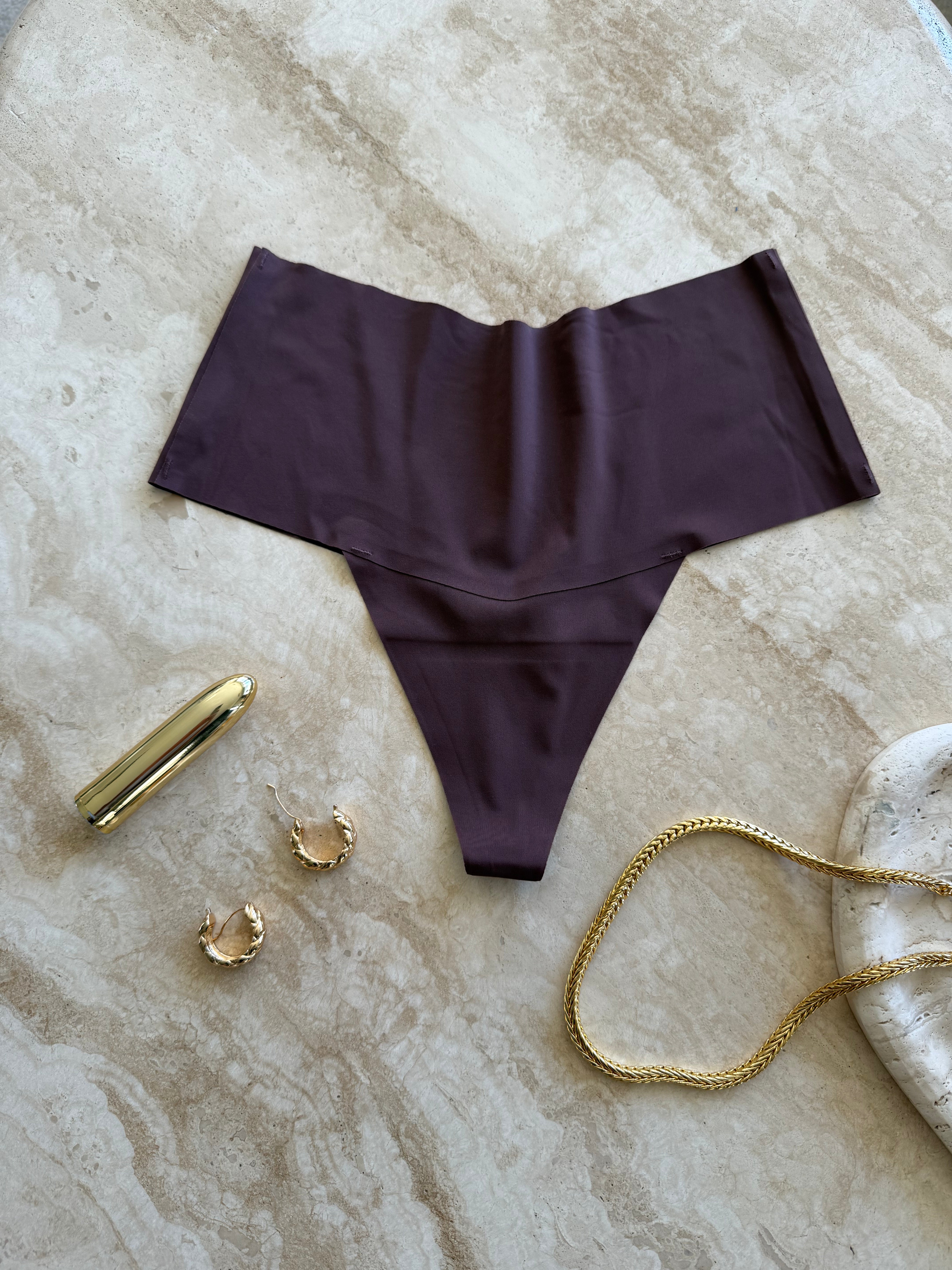 Detail view of The Kourtney Seamless Sports High Waist Thong in chocolate brown styled with gold jewelry on marble surface – minimalist still life by SELF Seductions