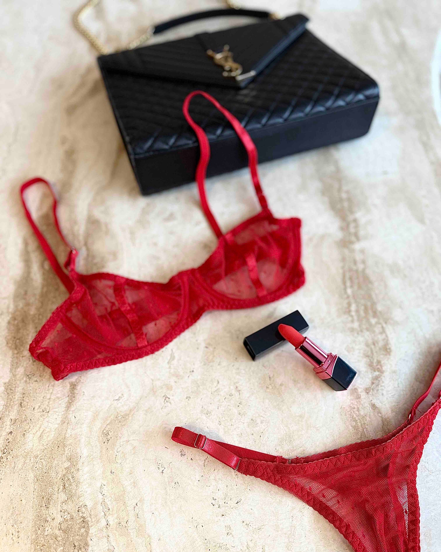 Red sheer mesh lingerie set with bra and thong styled on marble surface with black quilted bag and red lipstick, curated Valentine look by SELF Seductions.
