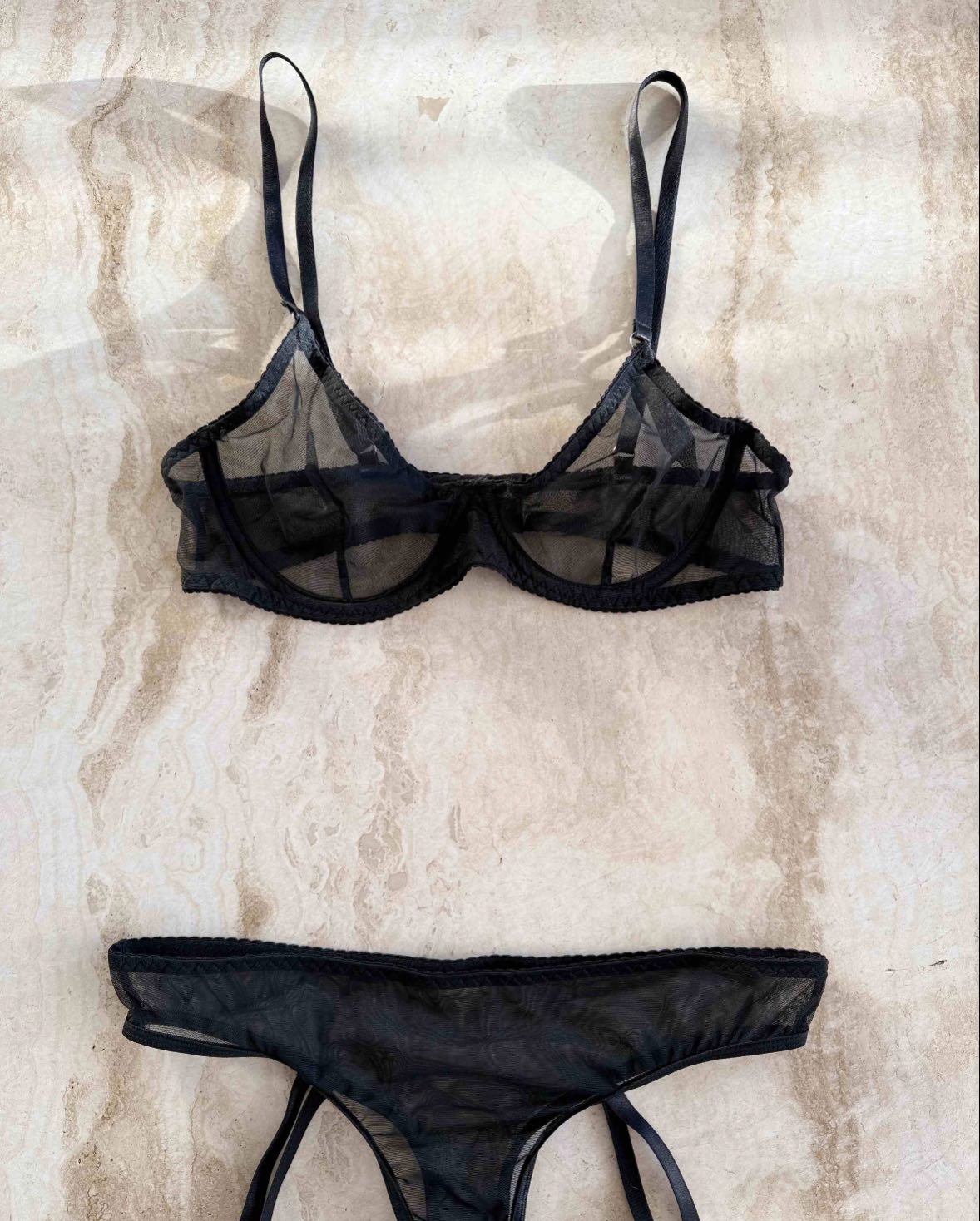 svart mesh bh och antydan til trosa i neutralt vacker ljus, fotograferat mot ett stenbord