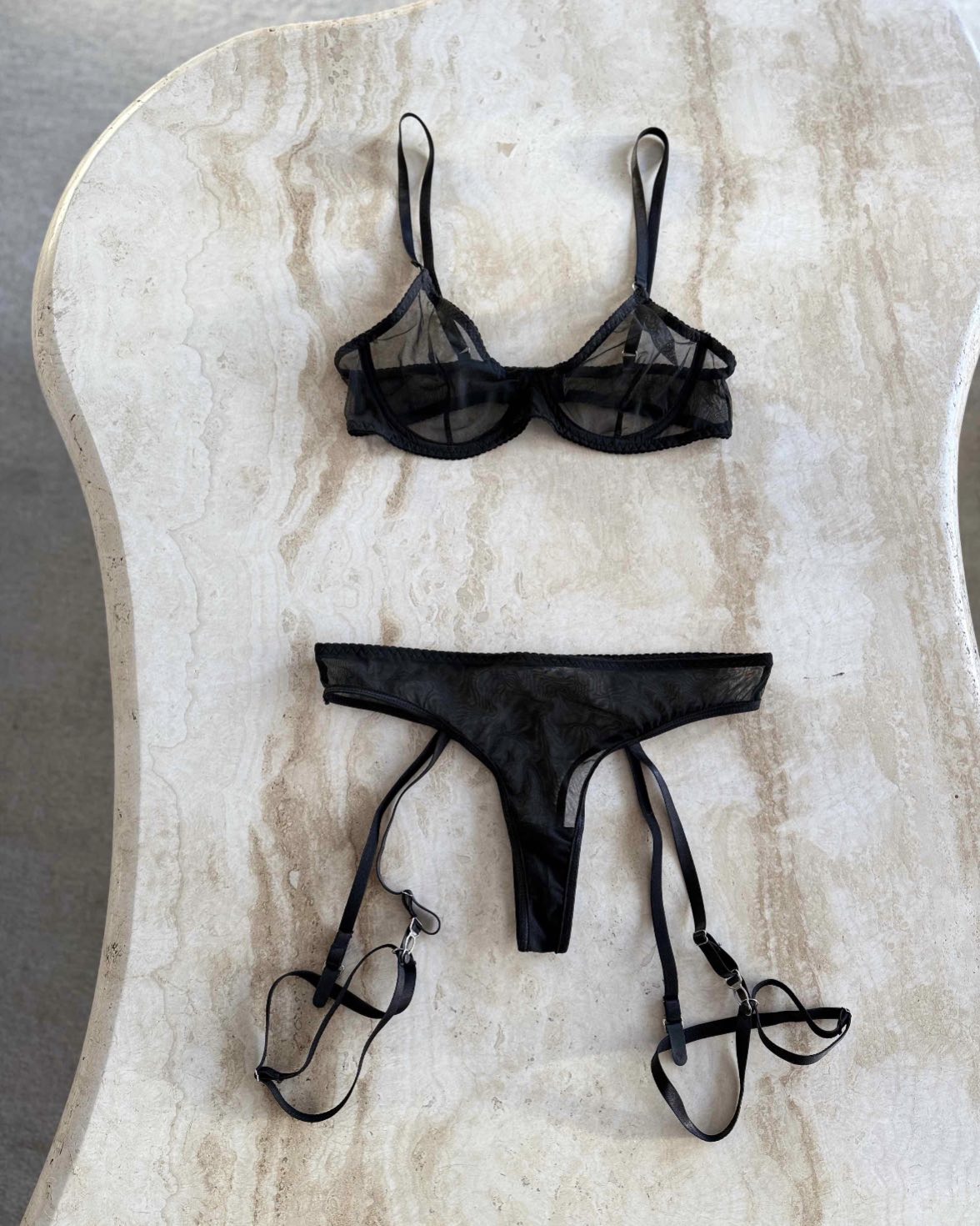 svart mesh bh och trosa i neutralt vacker ljus, fotograferat mot ett stenbord