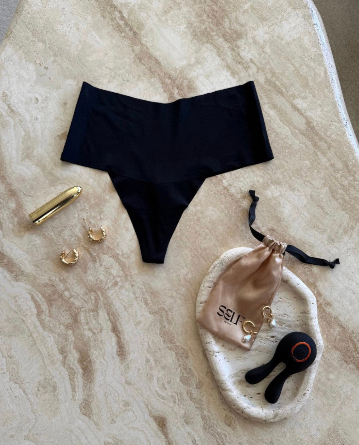 Black seamless high-waist thong with gold jewelry on marble surface – bold yet minimal lingerie still life by SELF Seductions