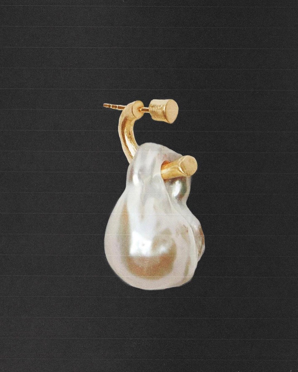 Close-up of a baroque pearl and gold earring on a dark textured background – SELF Seductions jewelry collection.