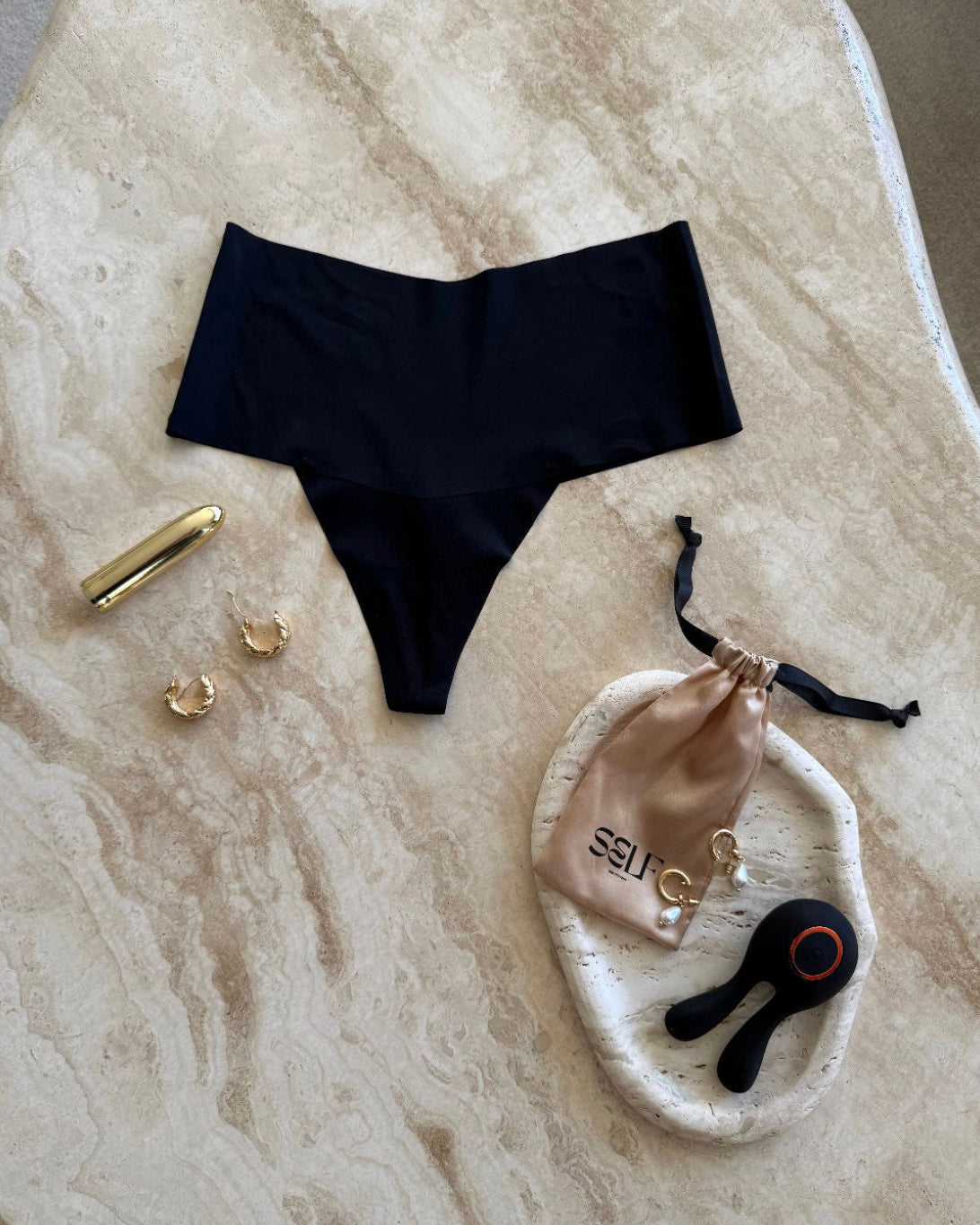 Black seamless high-waist thong with gold jewelry on marble surface – bold yet minimal lingerie still life by SELF Seductions