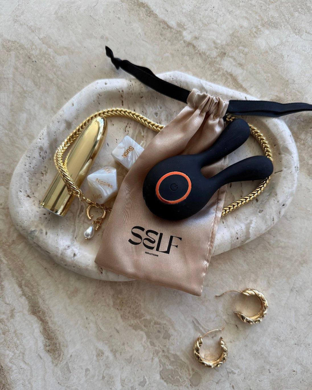 Black twin-ear silicone massager displayed on marble tabletop with gold jewelry and wellness accessory – elegant, sensual still life by SELF Seductions