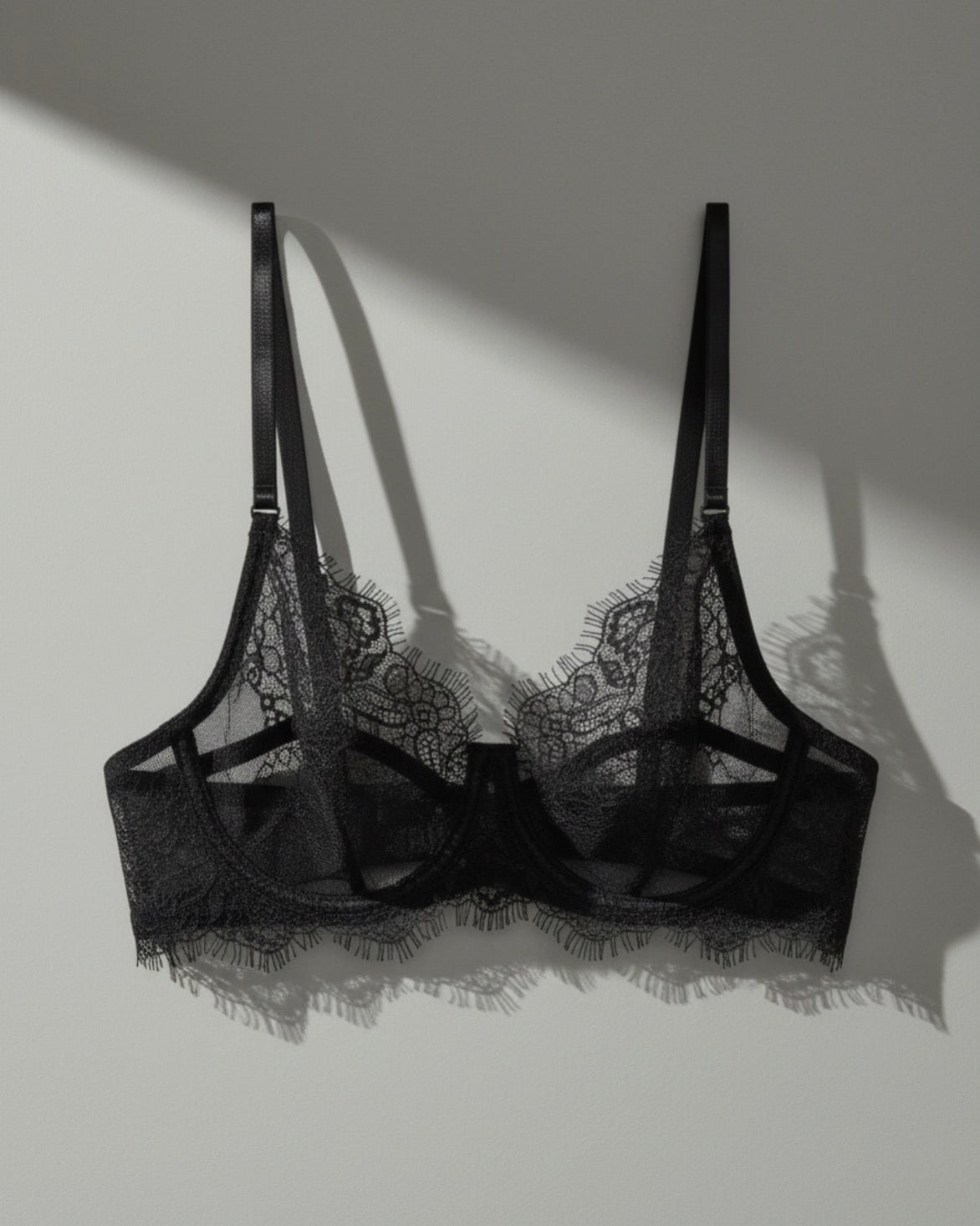 Black lace bralette in soft stretch lace, photographed in studio with natural light coming from the left, creating gentle shadows and a sense of depth against a neutral background.
