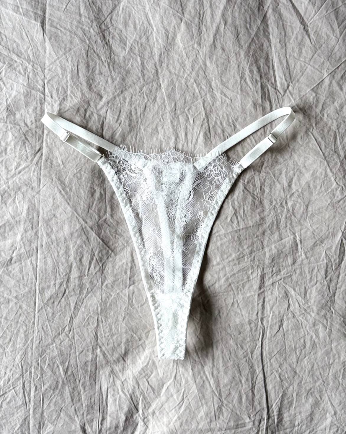 The Emma Soft Stretch Lace Thong in white – delicate lace lingerie styled on softly wrinkled linen bedding by SELF Seductions